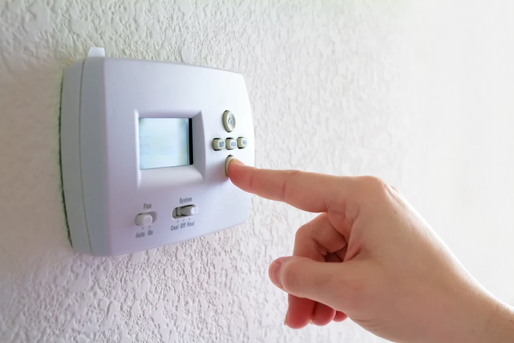 Hand adjusting a home thermostat related to aux heat operation during cold weather