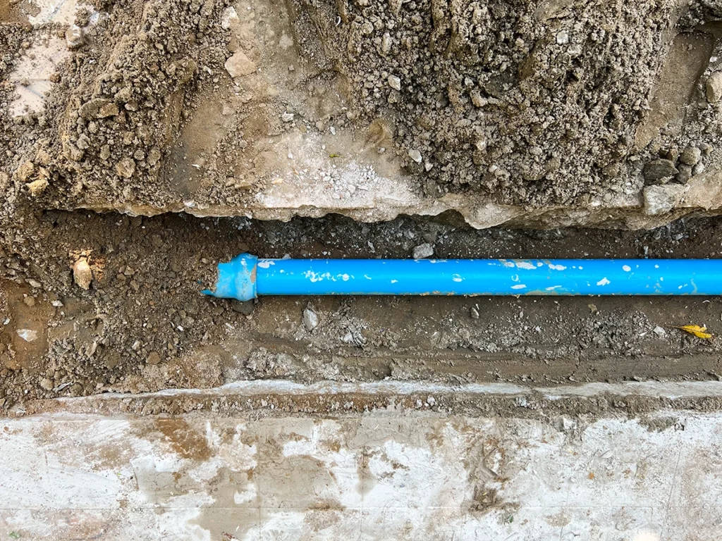 Gas line repair north shore MA: exposed blue underground water line in a trench during plumbing repair or installation